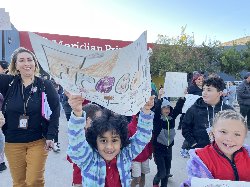 Students and adults walk and sing in front of the school